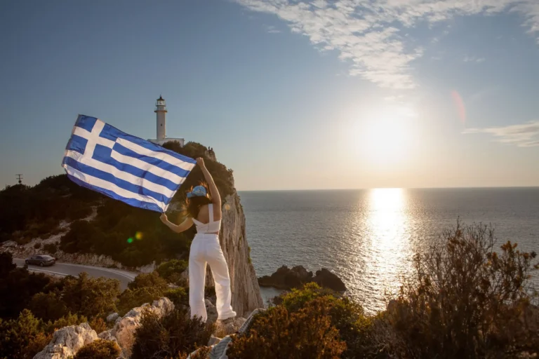 femme avec drapeau grec regardant le coucher du soleil au-dessus de la mer